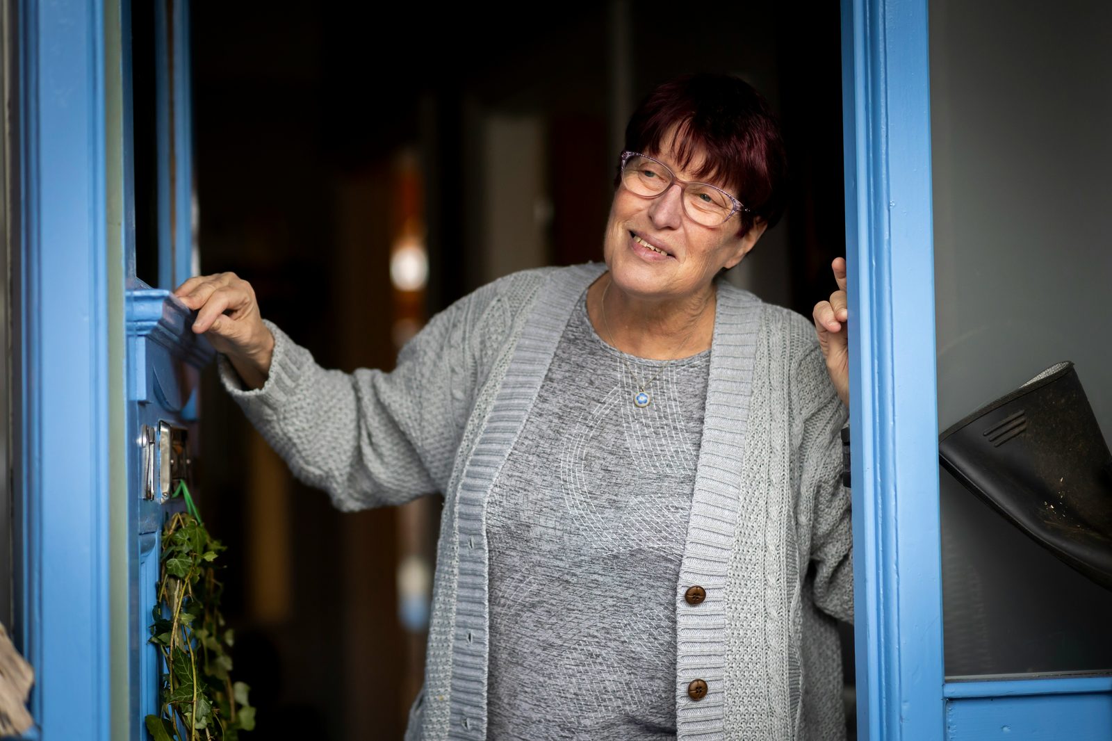 A woman smiling warmly as she opens her front door to welcome a visitor