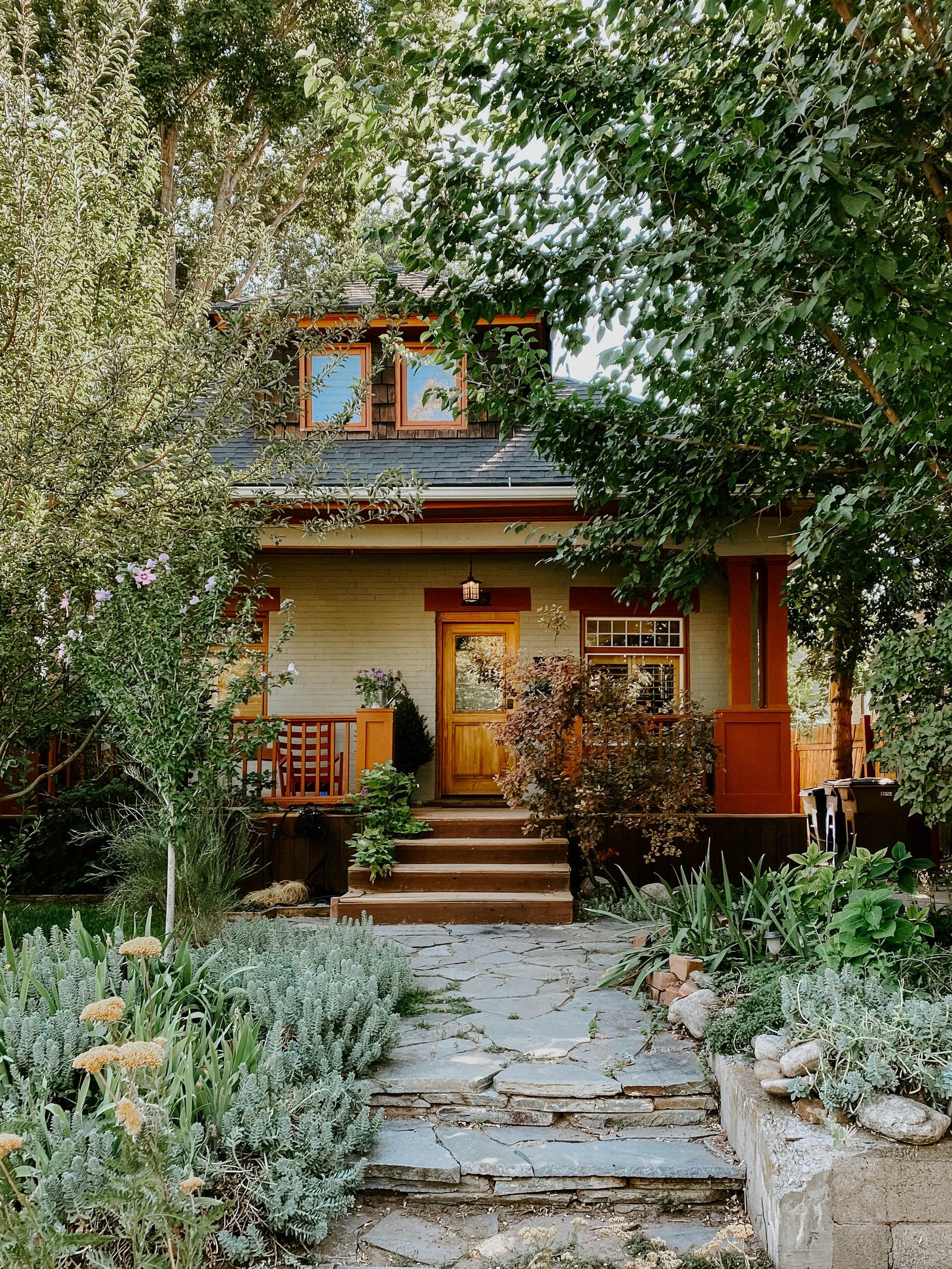 A craftsman home nestled in lush gardens with a stone path leading to the front door