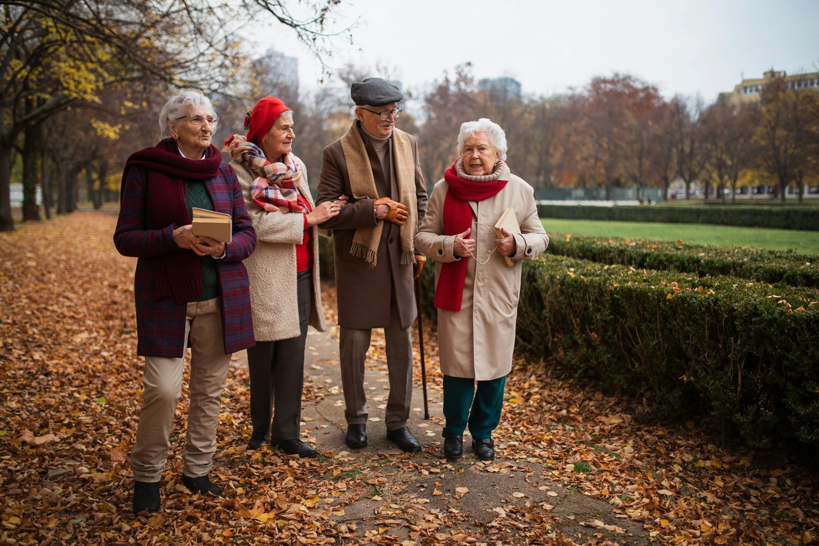 Four older adults walking together in an autumn park, sharing a warm conversation