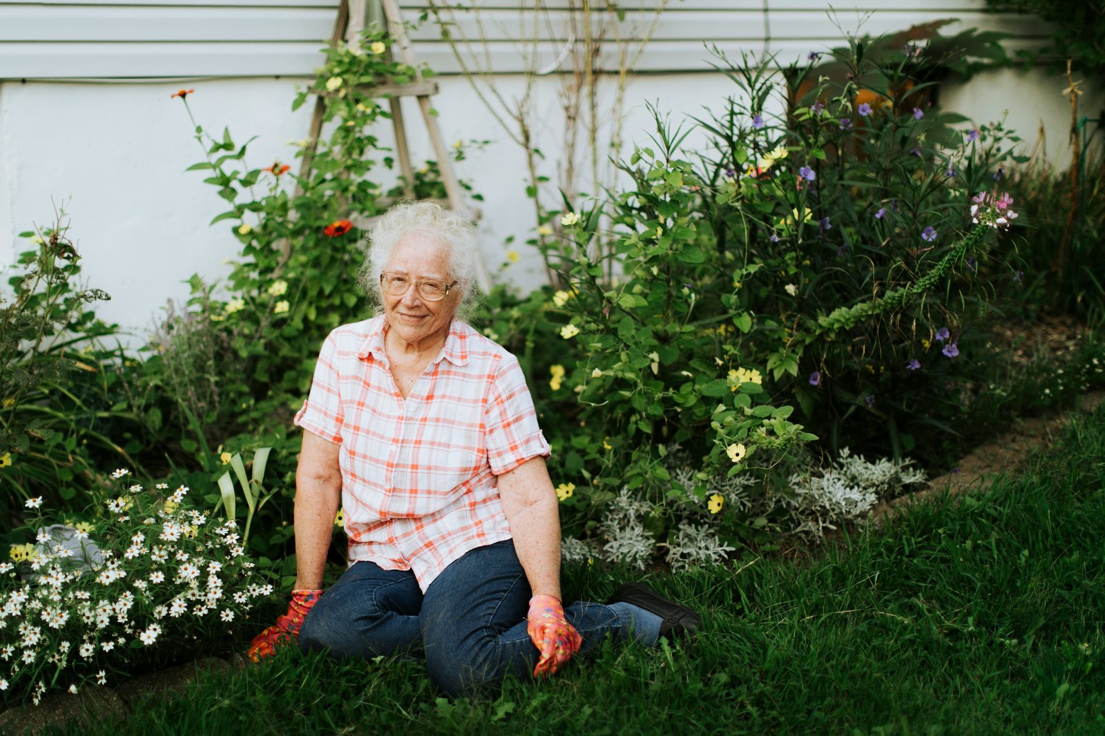 An older woman smiling while tending to her garden at home, surrounded by colorful flowers